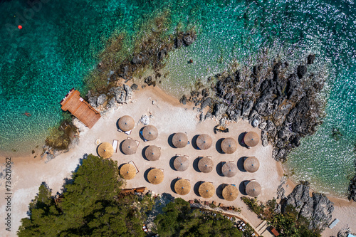 
A top-down view of the rocky coastline of a luxury resort with reed umbrellas and deckchairs for sunbathing.