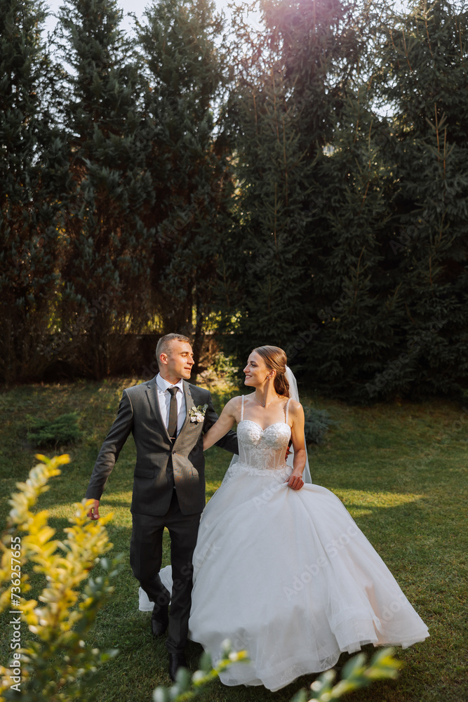 A wedding couple is walking in nature on an autumn day. Happy young bride and elegant groom holding hands. A stylish couple of newlyweds on their wedding day.