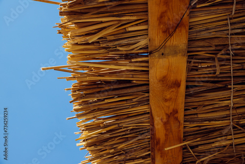 dry reed roof texture, thatched roof, palapa roof in blue sky. Wooden beach sun summer canopy. View from below