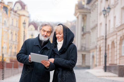 Attractive mature couple standing in urban street reading information on a tablet computer with a smile