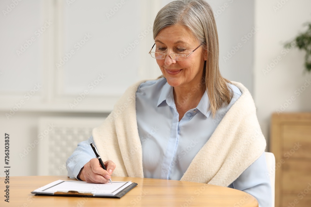 Smiling senior woman signing Last Will and Testament at table indoors Smiling senior woman signing Last Will and Testament at table indoors