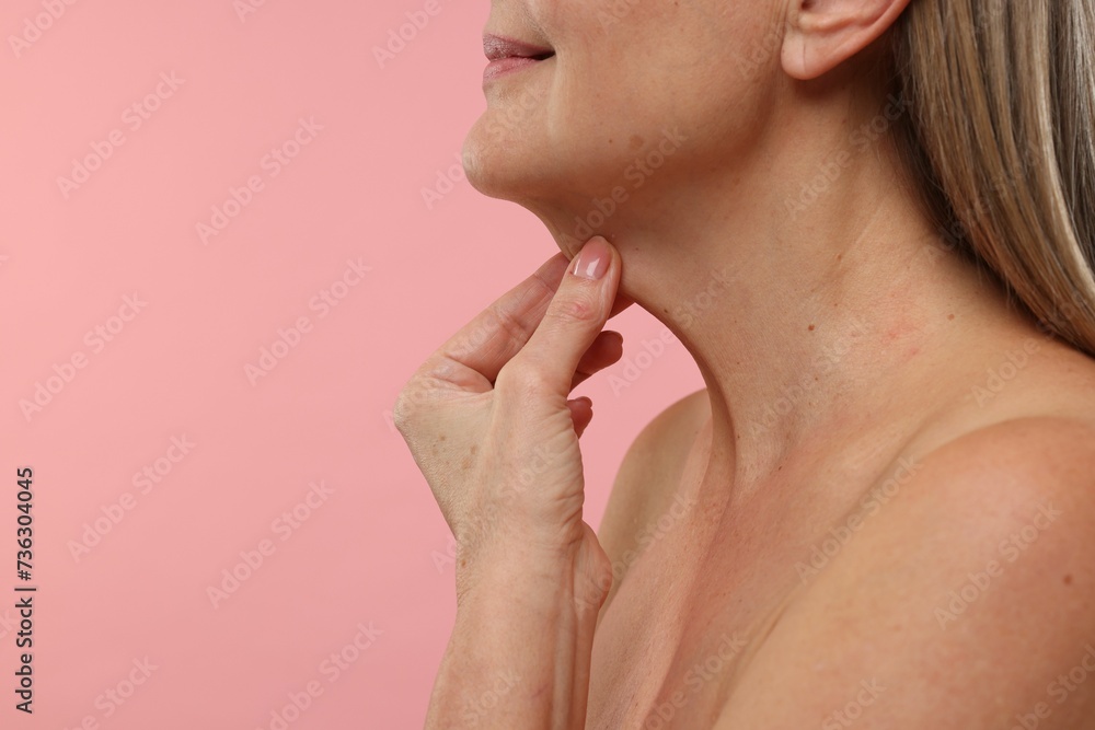 Obraz premium Mature woman touching her neck on pink background, closeup. Space for text