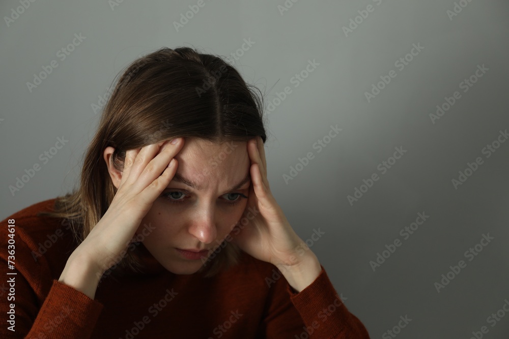 Sad young woman near grey wall indoors, space for text Sad young woman near grey wall indoors, space for text
