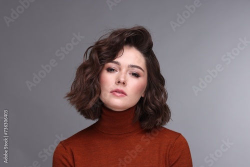 Portrait of beautiful young woman with wavy hairstyle on grey background