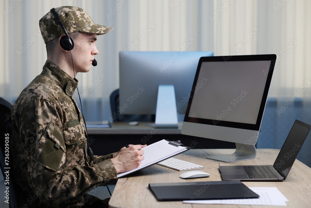 Military service. Young soldier with clipboard and headphones working at table in office