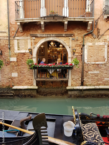 Gondola on a canal and a restaurant with an open balcony and flowers in Venice