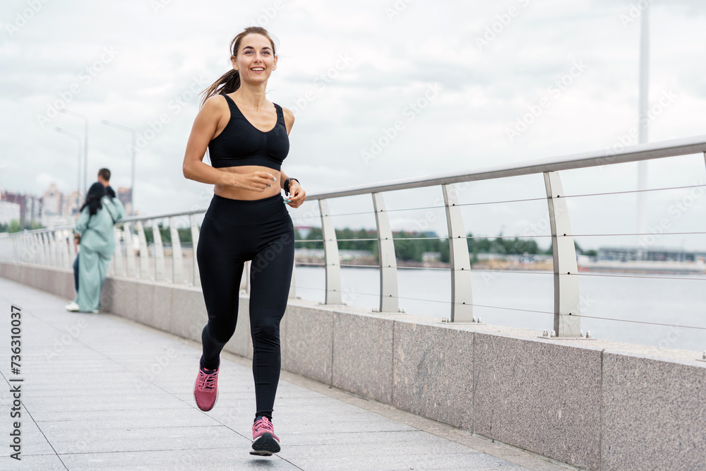 Female runner with a bright smile enjoying a run along the city's waterfront. Female runner with a bright smile enjoying a run along the city's waterfront.