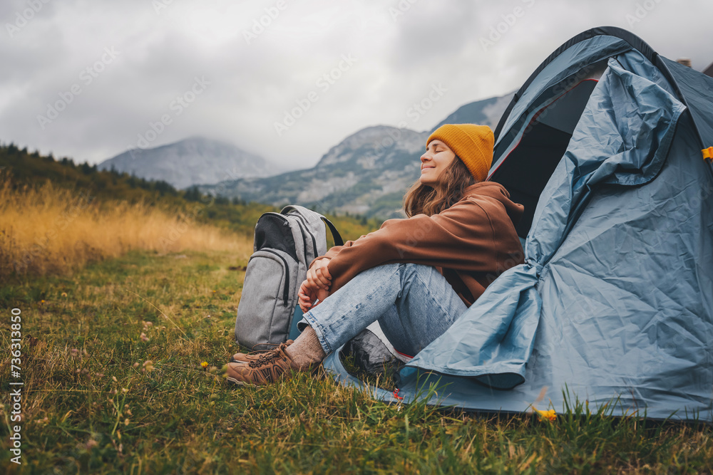 Young woman enjoying landscape sitting in the tent alone, engoy nature and relax. Traveling and camping concept. Camping tent