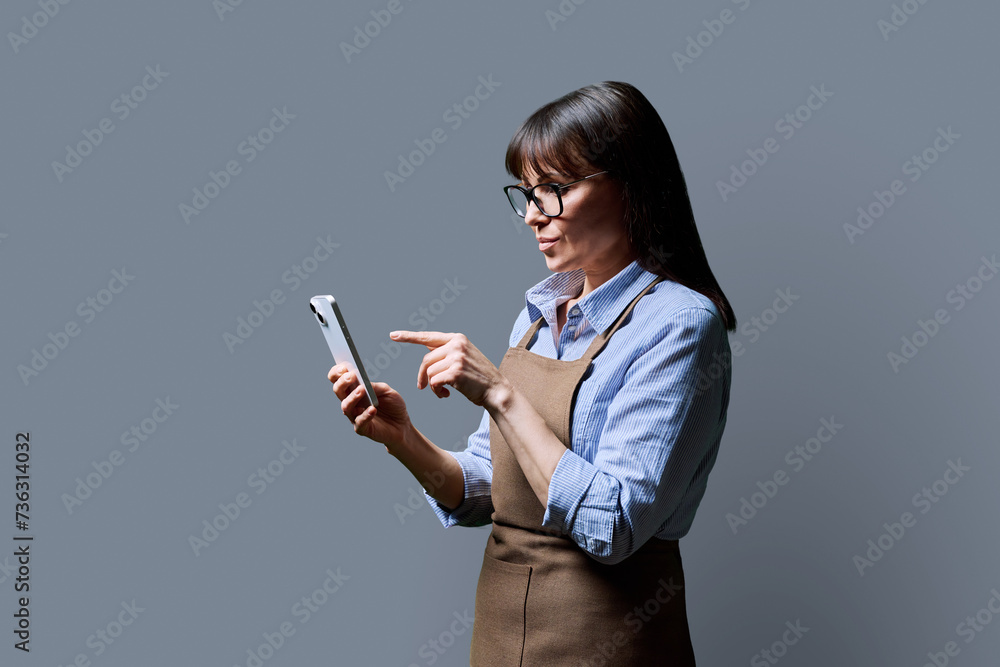 Business woman owner worker in an apron using smartphone, on gray background Business woman owner worker in an apron using smartphone, on gray background