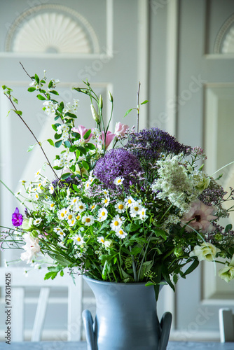 Blumenstrauss in einer Vase aus Keramik vor einem SChrank aus Holz. Frühlingsblumen: Kamille, Eustoma, Anemone, Spirea, Allium, Strandflieder, Zweige