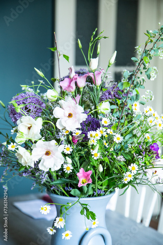 Blumenstrauss in einer Vase aus Keramik vor einer petrolfarbenen Wand. Frühlingsblumen: Kamille, Eustoma, Anemone, Spirea, Allium, Strandflieder, Zweige