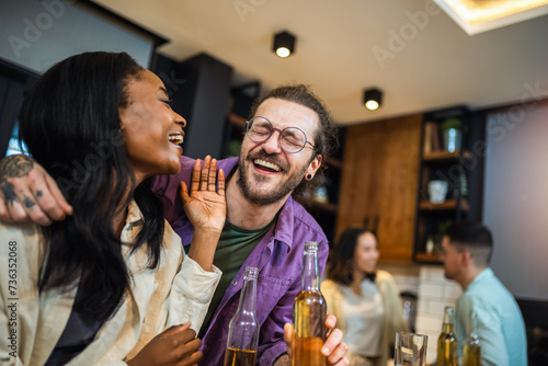 Two diverse young friends laughing together during a dinner together in a friend's kitchen