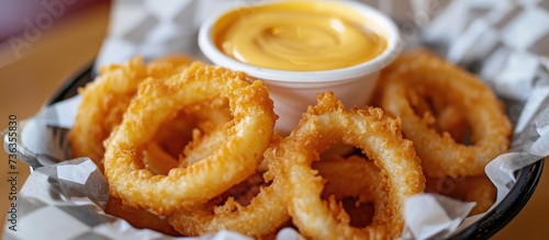 Battered onion rings and cheese sauce in a basket.