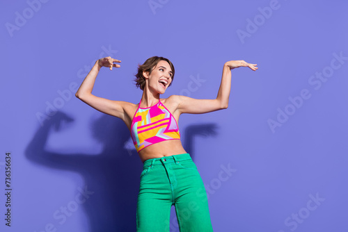 Photo of positive adorable shiny woman stylish bright clothes dance with raised hands look empty space isolated on purple color background