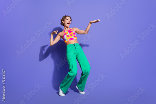 Photo of cheerful adorable carefree girl dressed stylish clothes standing tiptoes looking empty space isolated on purple color background