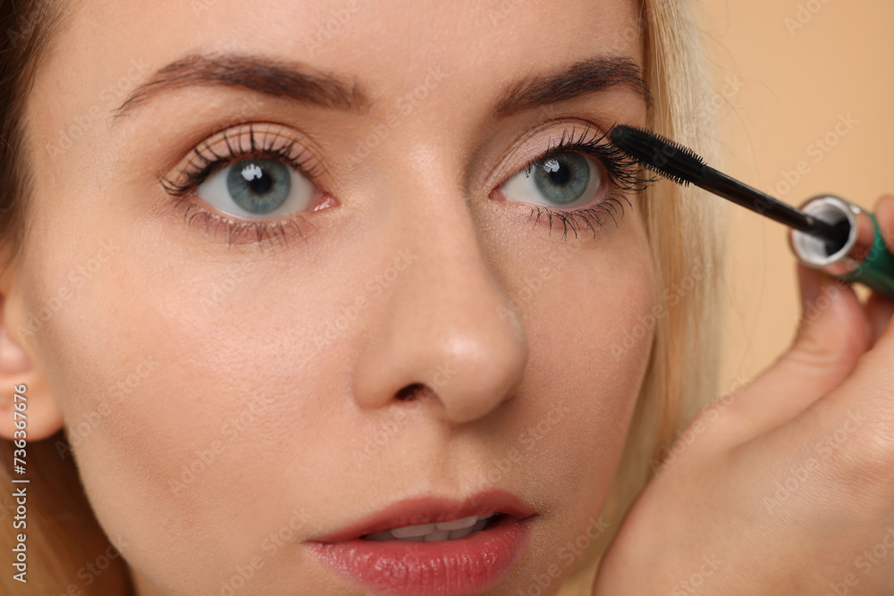 Beautiful woman applying mascara on beige background, closeup