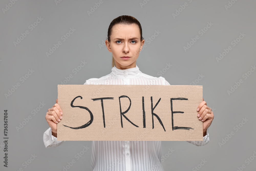 Woman holding cardboard banner with word Strike on grey background Woman holding cardboard banner with word Strike on grey background
