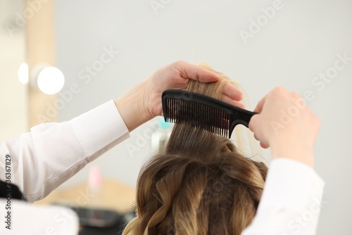 Hair styling. Hairdresser combing woman's hair indoors, closeup