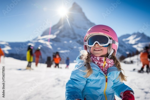Little girl snowboarder with equipment helmet and goggles outwear holding snowboard resting on top of ski slope in sunlight
