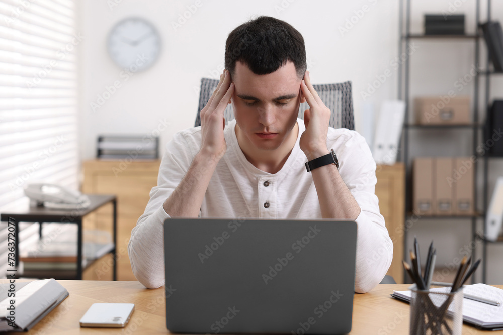 Young man suffering from headache at workplace in office Young man suffering from headache at workplace in office