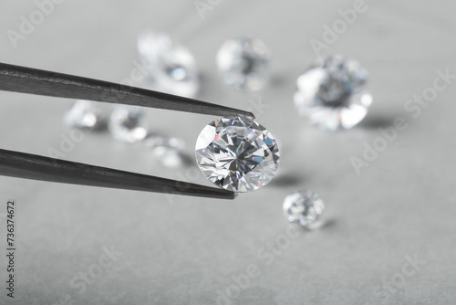 Tweezers with beautiful shiny diamond above light gray table, closeup. Space for text