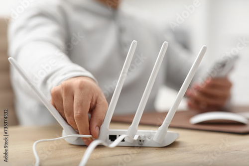 Man inserting cable into Wi-Fi router at wooden table indoors, closeup