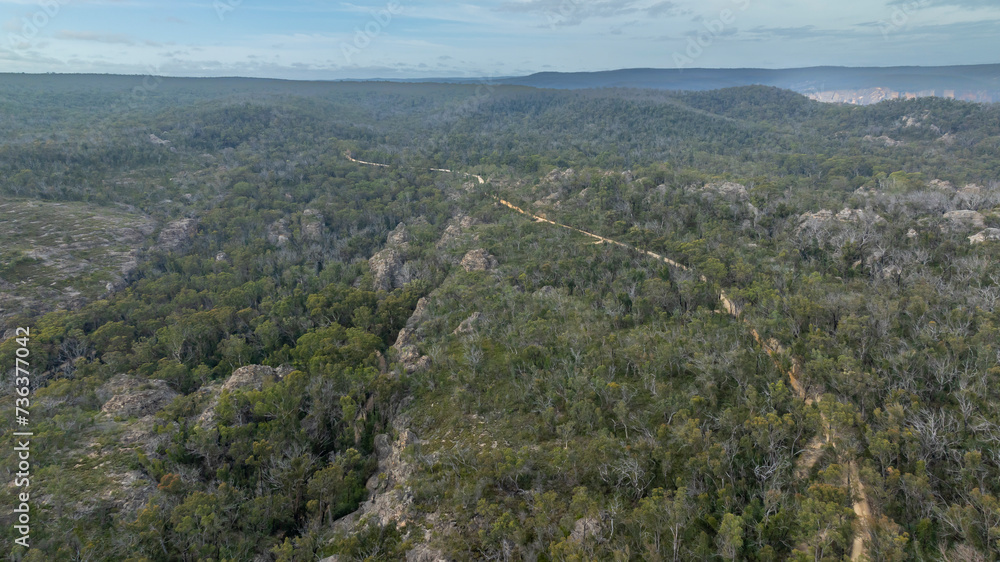 Drone aerial photograph of a long and narrow vehicle dirt track running along a rocky mountain ridge in the Blue Mountains in New South Wales in Australia