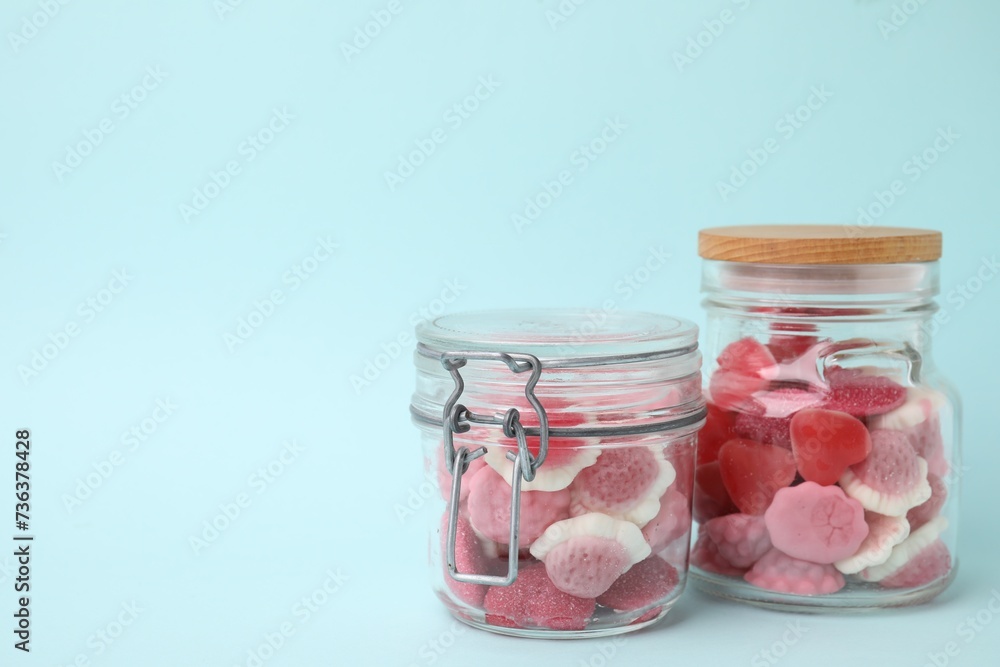 Tasty pink candies in glass jars on light blue background, space for text Tasty pink candies in glass jars on light blue background, space for text