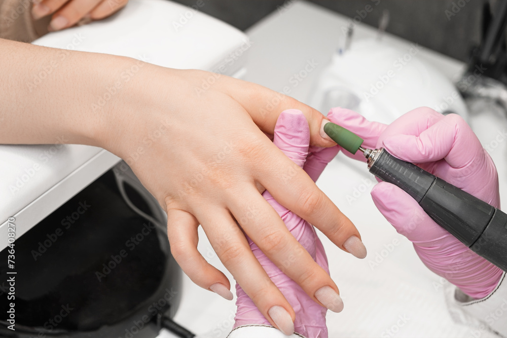 Nail technician polishing the cuticle with nail drill machine, preparing for the application of gel nail polish in a salon. Close up. Nail technician polishing the cuticle with nail drill machine, preparing for the application of gel nail polish in a salon. Close up.