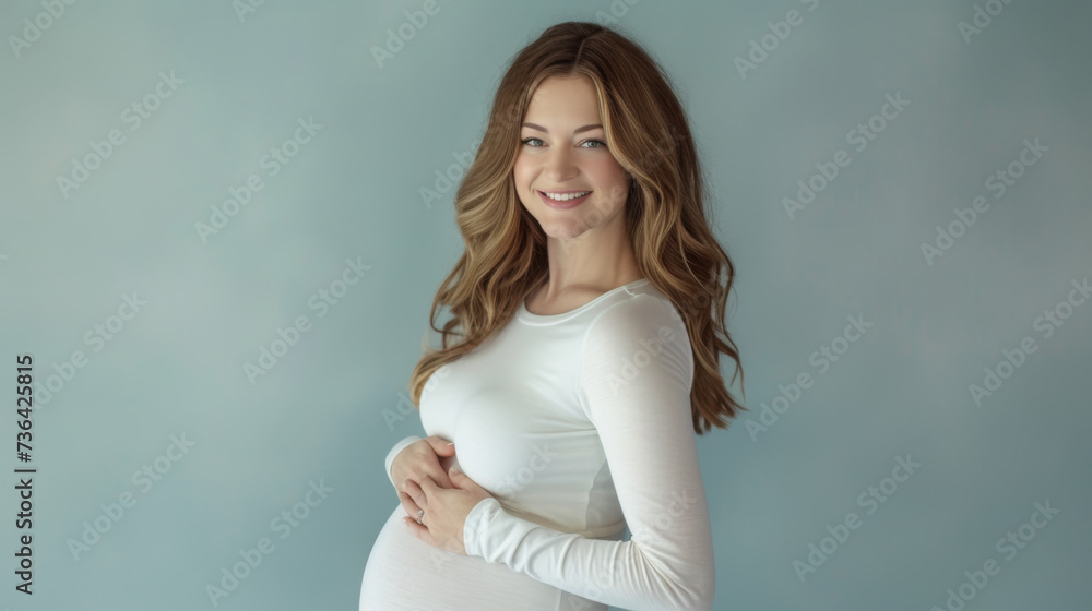 smiling pregnant woman in a white dress, holding her belly, standing against a soft blue background smiling pregnant woman in a white dress, holding her belly, standing against a soft blue background