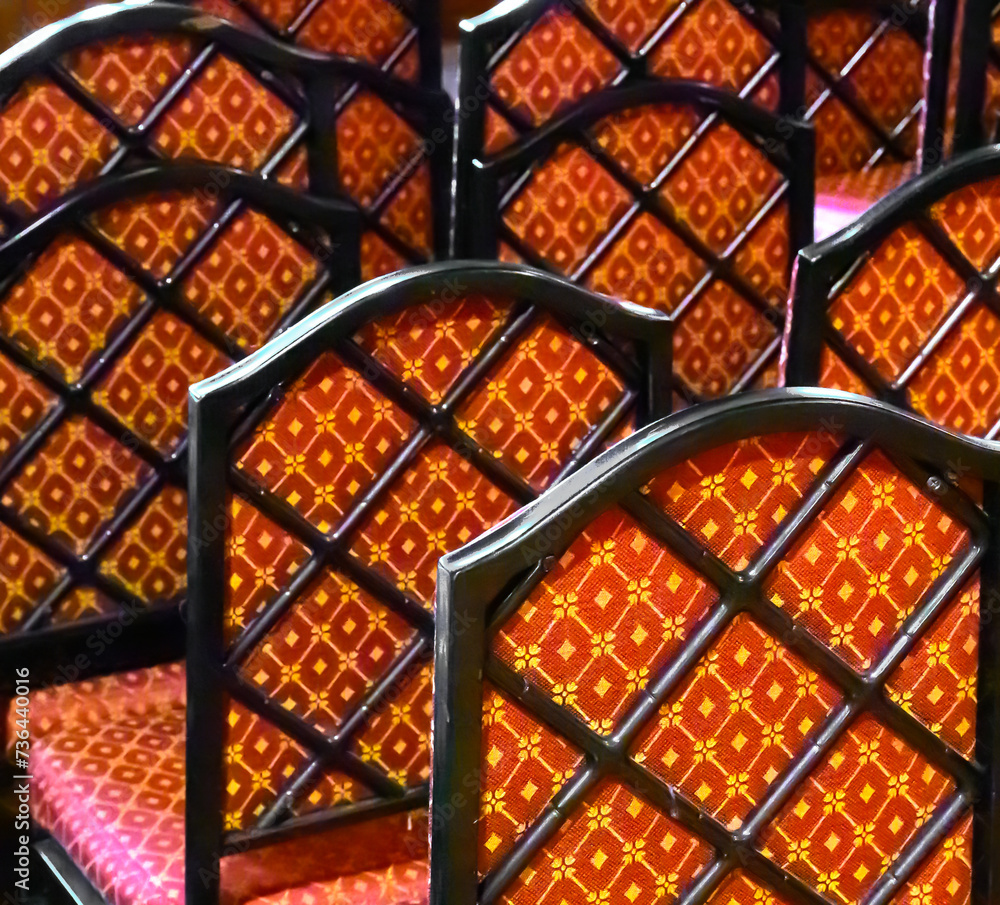A row of old antique chairs is set to the side of the room when unused. A unique pattern is made from these the red velvet pattern and the chair back designs. Repeating pattern in Chairs Upstate NY