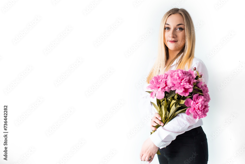 Woman holds peony flowers agains white wall. Young girl with spring summer bouquet bouquet. Lifestyle photo with flowers and a copy space.