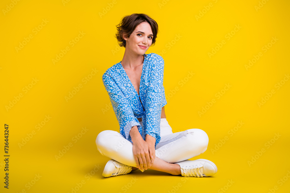 Full size photo of adorable pretty pleasant woman wear blue top white trousers sitting on floor isolated on yellow color background Full size photo of adorable pretty pleasant woman wear blue top white trousers sitting on floor isolated on yellow color background