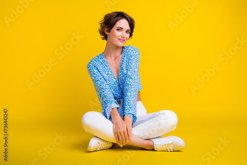 Full size photo of adorable pretty pleasant woman wear blue top white trousers sitting on floor isolated on yellow color background