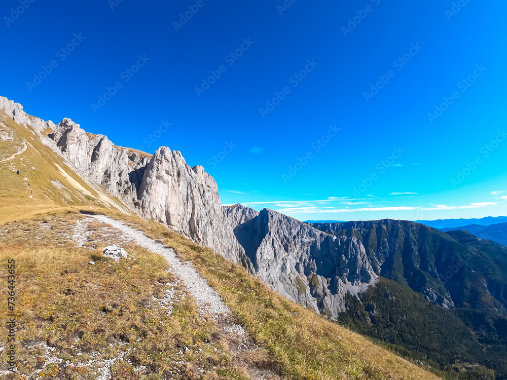 Idyllic hiking trail along golden alpine meadow with panoramic view of majestic Hochschwab massif, Styria, Austria. Wanderlust in remote Austrian Alps. Sense of escapism, peace, personal reflection