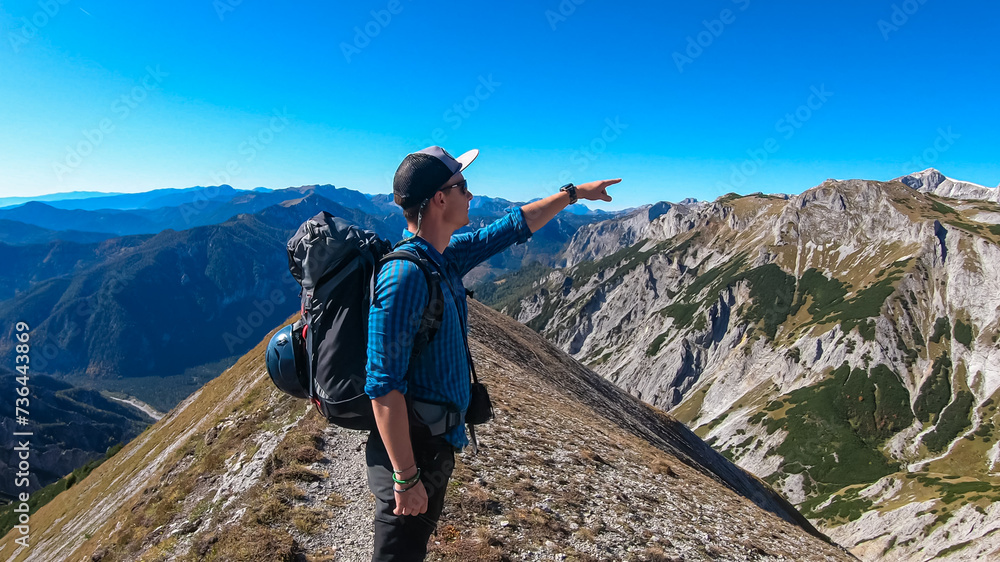Hiker man pointing finger on idyllic hiking trail on alpine meadow with scenic view of majestic Hochschwab mountain range, Styria, Austria. Wanderlust in remote Austrian Alps. Sense of escapism, peace
