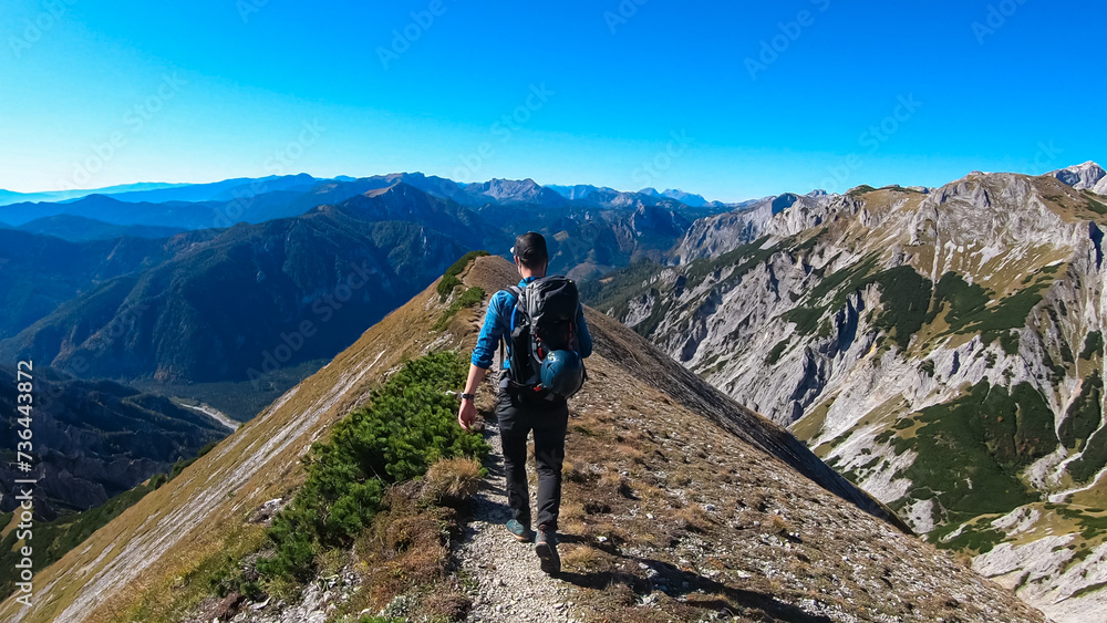 Hiker man on idyllic hiking trail on alpine meadow with scenic view of majestic Hochschwab mountain range, Styria, Austria. Wanderlust in remote Austrian Alps. Sense of escapism, peace, reflection