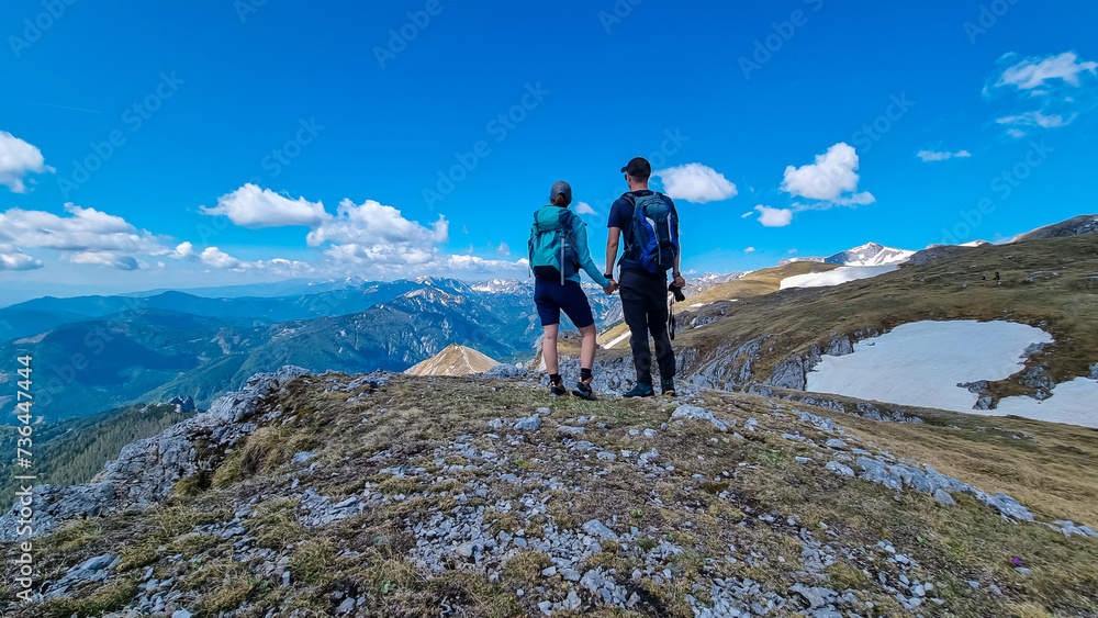 Hiker couple with panoramic view of majestic mountain peak Ringkamp in wild Hochschwab massif, Styria, Austria. Scenic hiking trail in remote Austrian Alps on sunny day. Wanderlust in alpine spring
