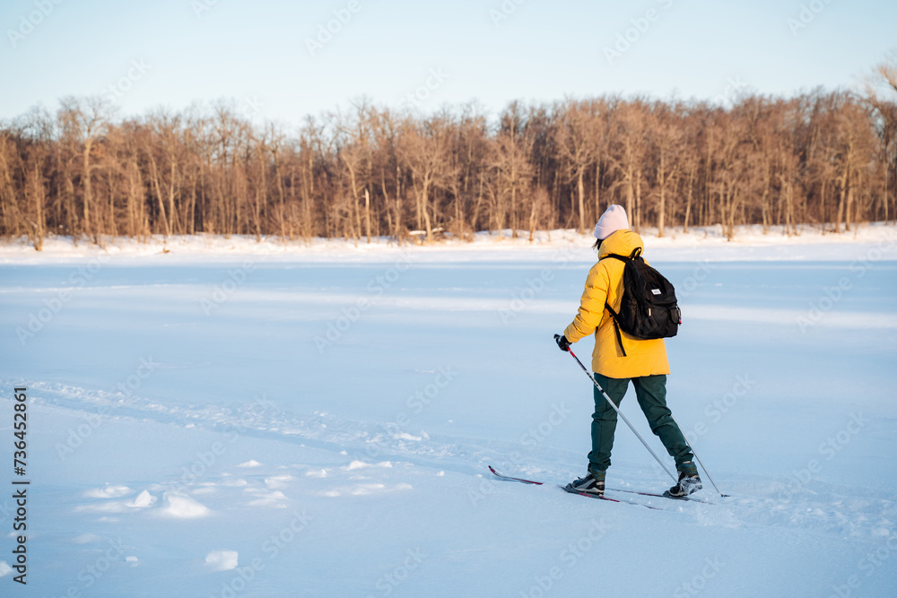 A man in a yellow jacket is skiing across snowy terrain under the sky