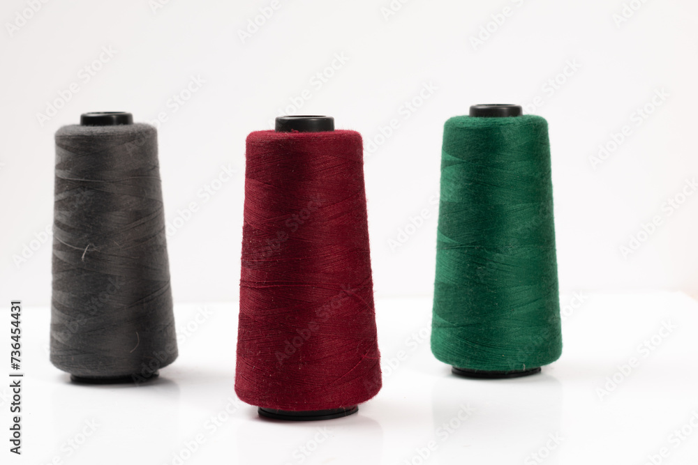 Sewing machine threads, red, green, gray, overlock thread. Industrial threads on a white background, spools of multicolored threads Sewing machine threads, red, green, gray, overlock thread. Industrial threads on a white background, spools of multicolored threads