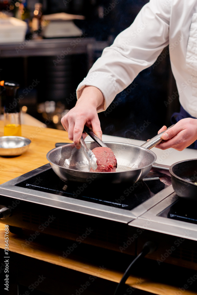 close-up of a chef's hand placing a beef steak on frying pan with tongs