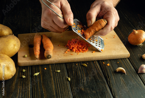 Grating carrots with a grater on a kitchen board. Chef hands preparing vegetable dishes in tavern kitchen photo