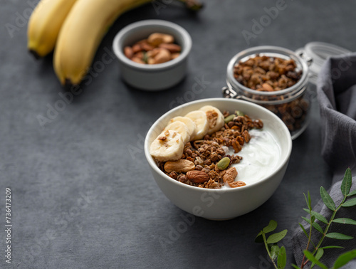 Healthy breakfast. Homemade granola with banana and nuts in a bowl on a dark  background close up.