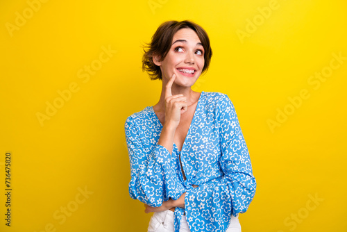 Photo of funky dreamy young woman wear flower print blouse finger chin looking empty space isolated yellow color background photo