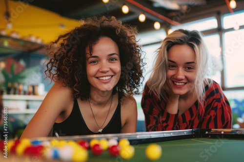 Joyful women gather around the pool table, cue sticks in hand, ready to sink the perfect shot and conquer the baize in this vibrant indoor recreation room photo