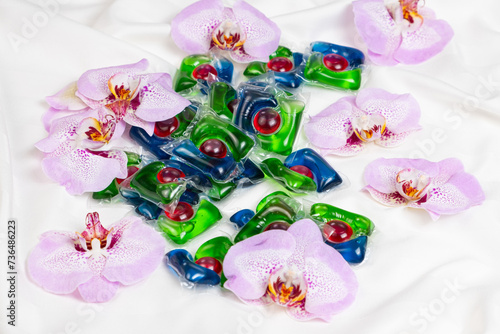 Laundry capsules among orchid flowers on satin fabric.