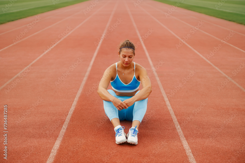 Fototapeta premium Woman sitting and relaxing on the running track at the sports arena