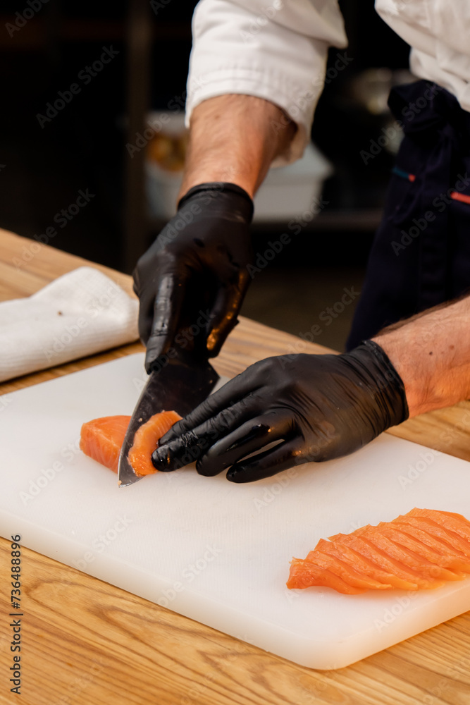 close-up of a chef's hands in black gloves cutting salmon fillet on white board
