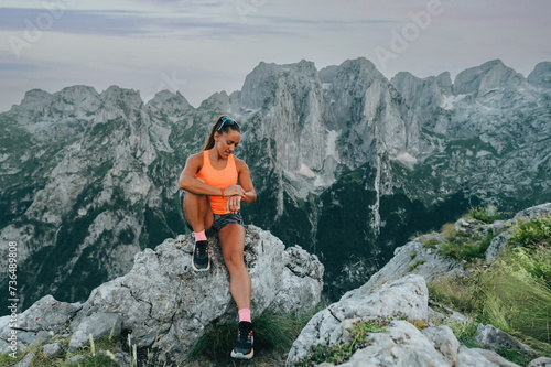 A skyrunner is sitting on a rock in mountain and looking at stopwatch.