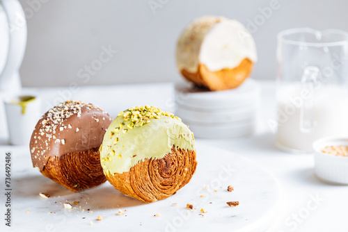 Fusion croissant called Cromboloni invented in New York. Round puff pastry filled with cream, and glazed with white, milk chocolate or pistachio. Crunchy and soft in the same time. Bright background.  © Haris